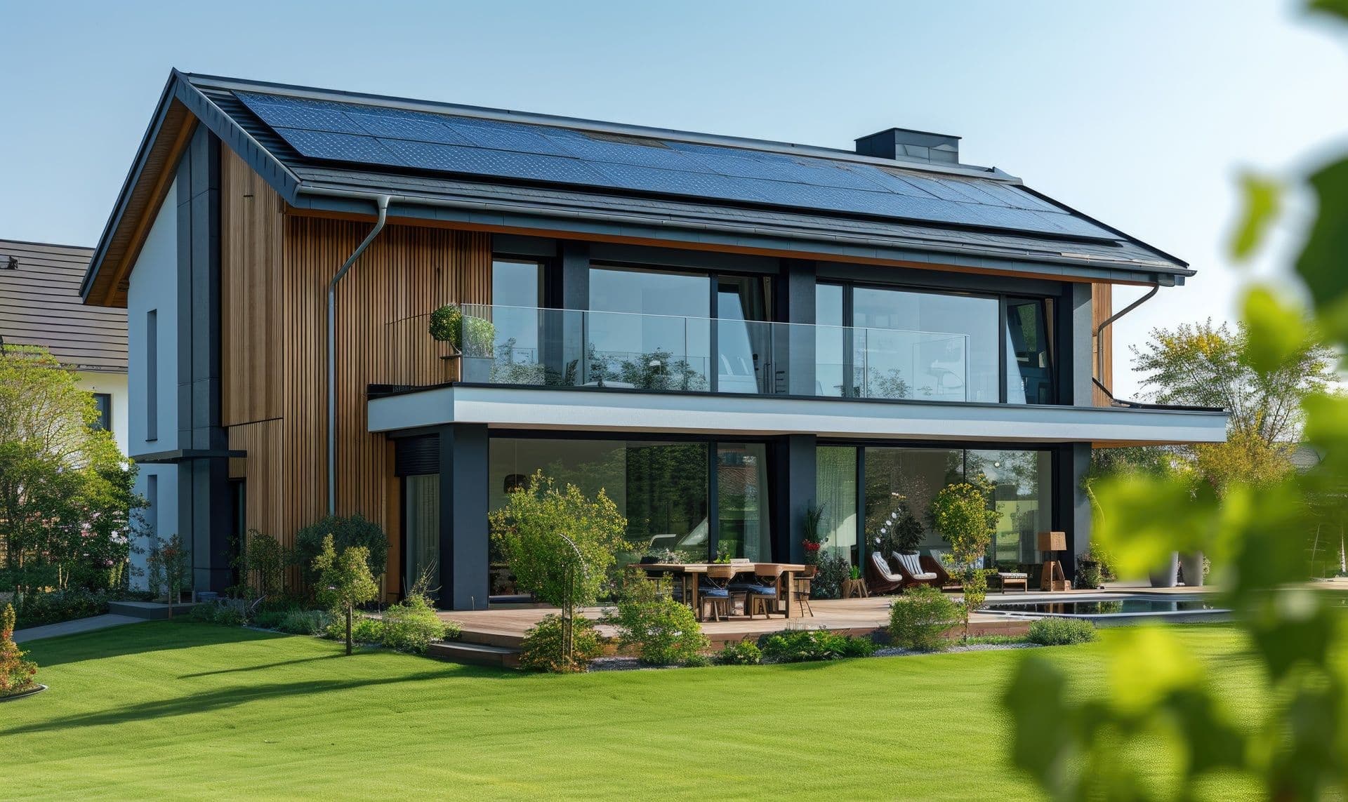 Modern two-story home with wood siding, large windows, a glass balcony, landscaped yard, and rooftop solar panels
