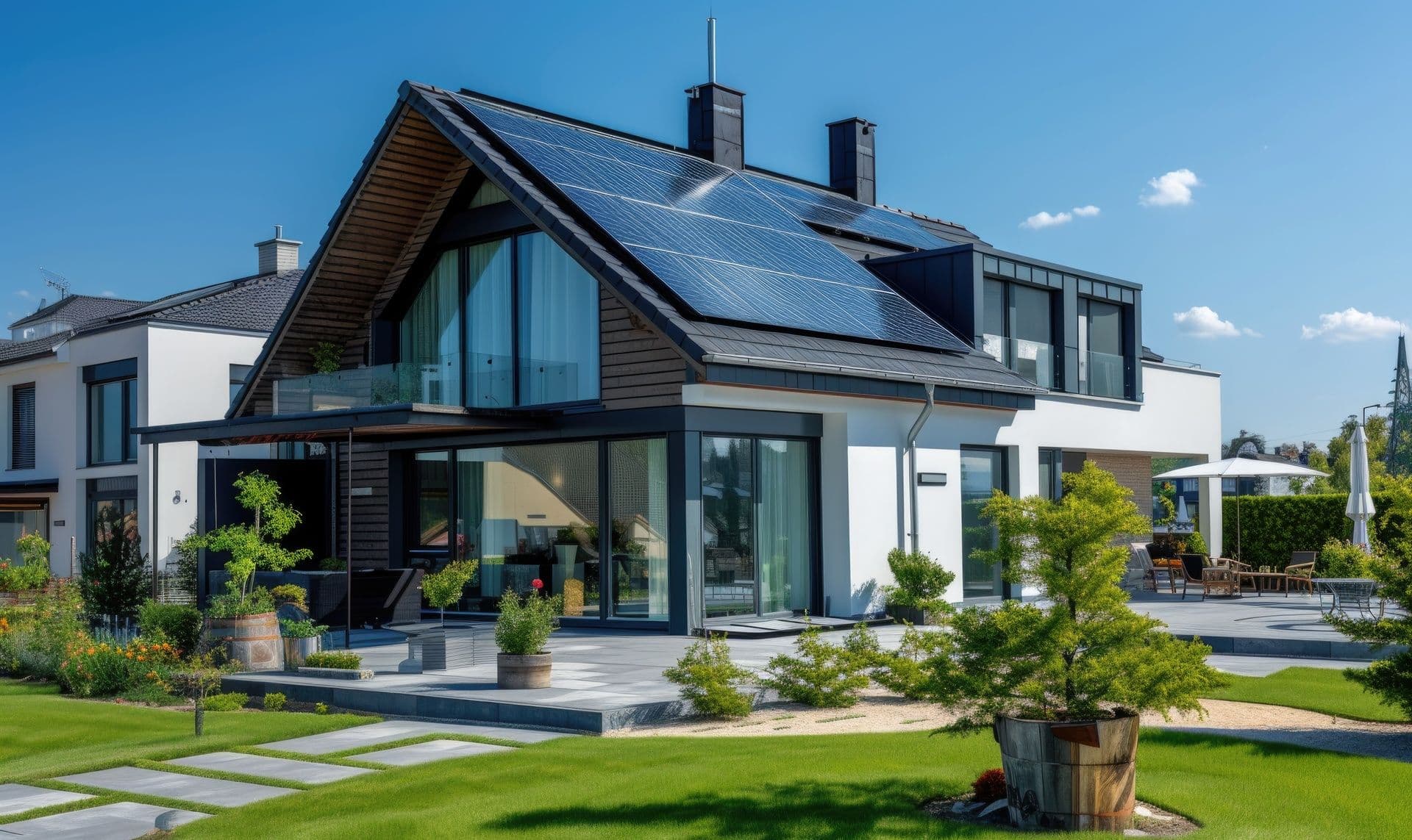 Contemporary two-story home with a steep roofline, large windows, outdoor patio, landscaped garden, and solar panels.
